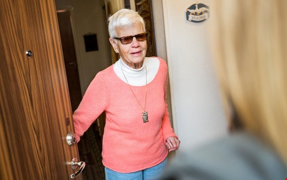 En äldre kvinna öppnar ytterdörren och välkomnar en instruktör på hembesök
