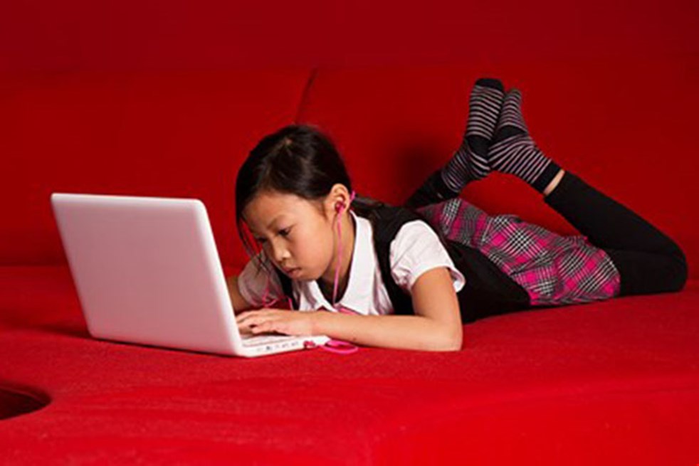 En flicka ligger framför en dator och läser något på skärmen.