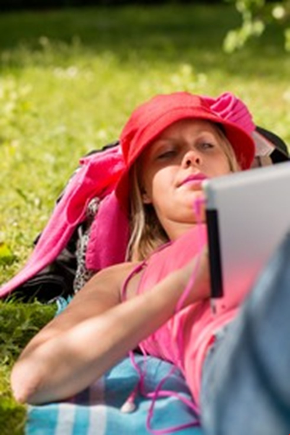 En ung kvinna ligger i gräset på en filt och surfar på en läsplatta