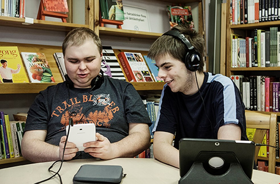 Två killar läser talböcker på ett bibliotek.