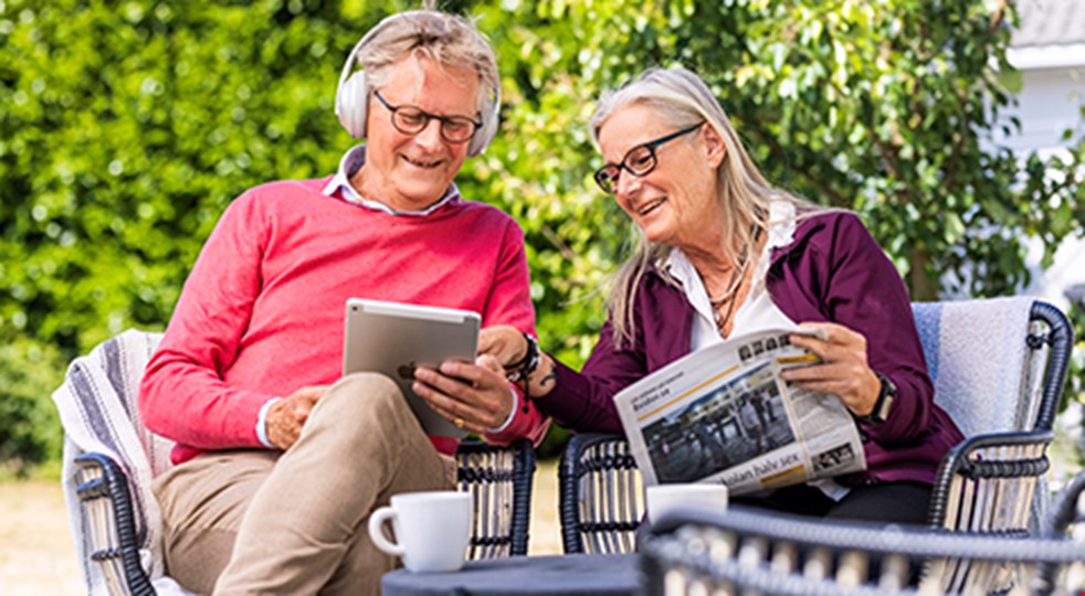 En man och en kvinna läser dagstidningen som taltidningen i sin trädgård.