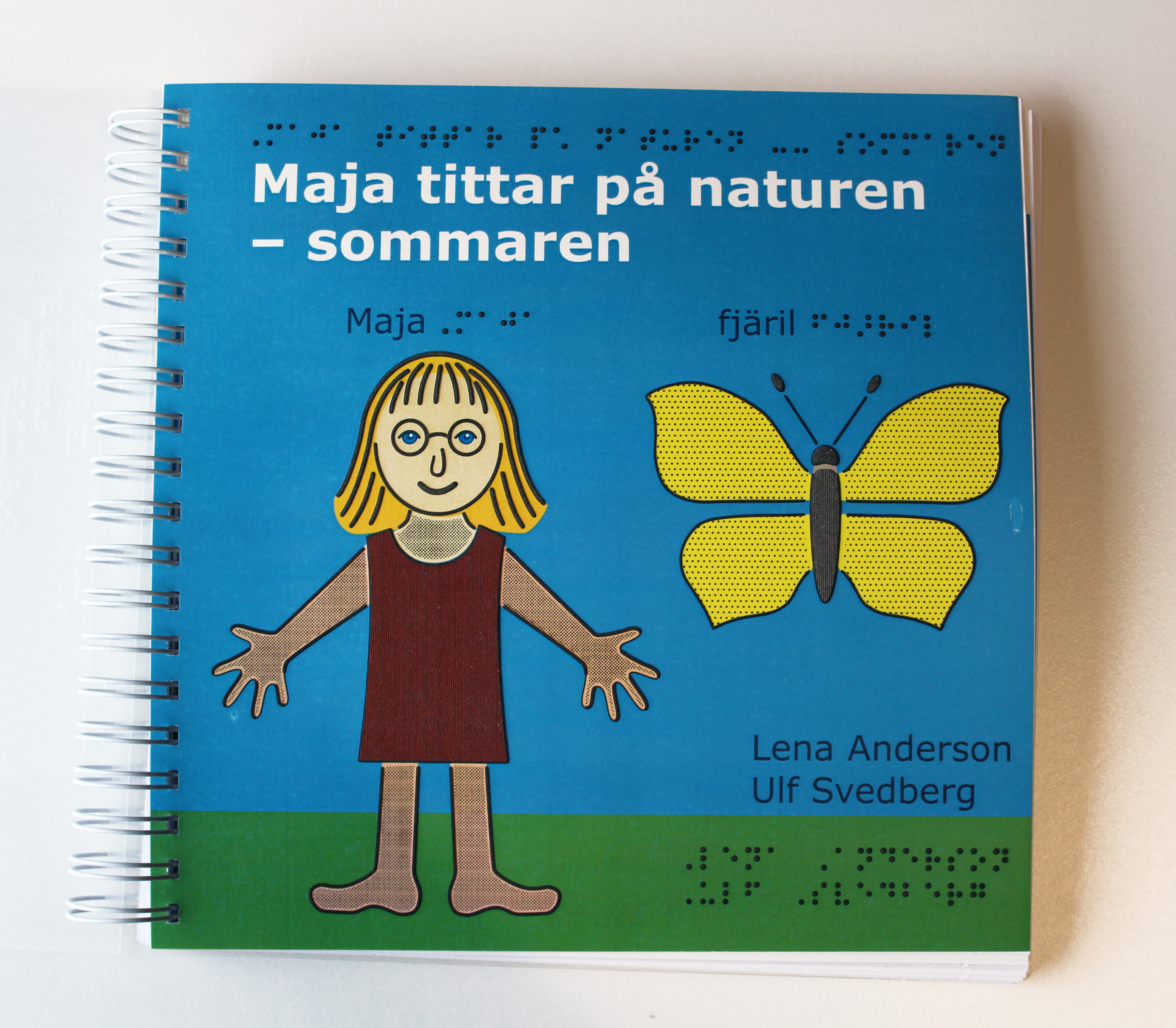 Bilden visar omslaget till den taktila boken. Omslaget visar en blå bakgrund. Det finns också en tjej med bruna kläder och en gul fjäril.