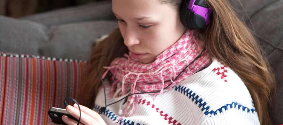 En flicka med hörlurar som lyssnar på en talbok i mobilen.