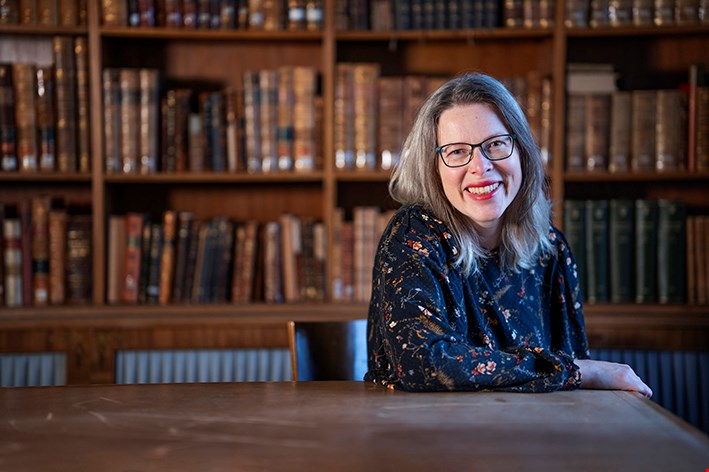 Lynn Alpberg sitter lutad mot ett bord i ett gammalt bibliotek. Bokhyllorna bakom henne är i mörkt trä och böckerna gamla.
