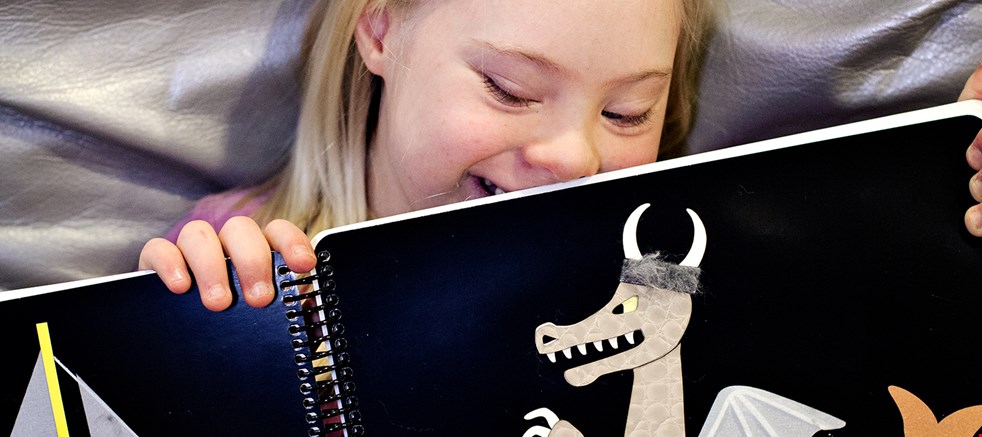 Ung flicka med Downs syndrom läser en punktbok.